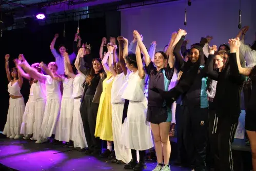 A group of students, on a stage, holding hands in celebration.